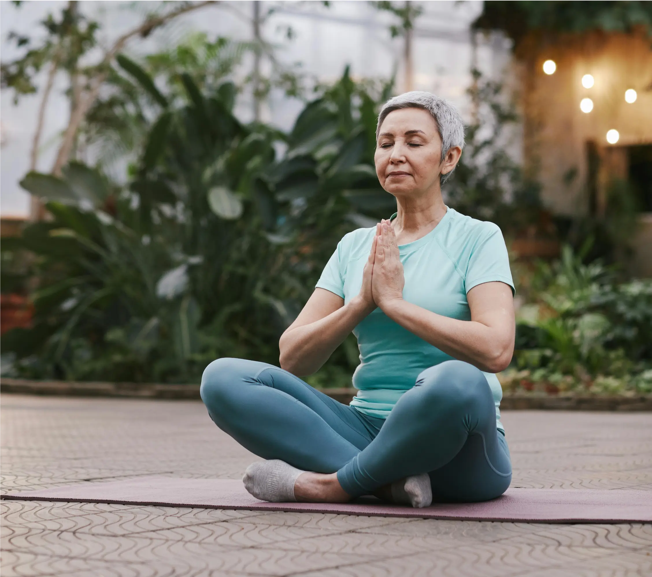 An older woman sitting cross-legged with her palms together.